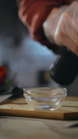 A cook is carefully pouring a rich sauce into a small bowl, focusing on flavor development while preparing gourmet burgers in a stylish kitchen. The atmosphere is vibrant and culinary