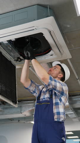 Technician repairing air conditioner unit on ceiling