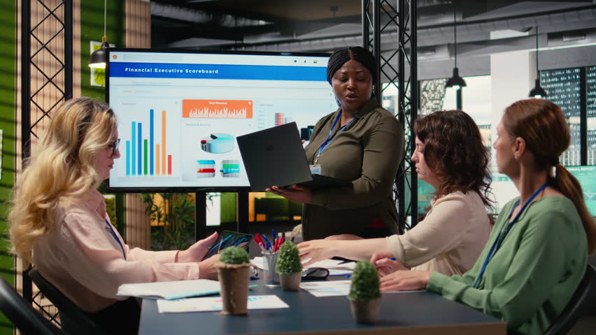 Executive manager presenting financial situation on a TV monitor, discussing about development and problem solving ideas with her colleagues. All female team in a briefing session. Camera A.
