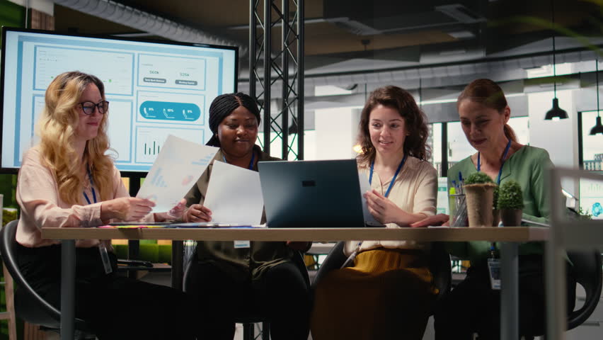 Group of businesswomen engaging in collaboration during briefing session, analyzing data and writing reports while embracing a mindset of growth. Goals oriented meeting. Camera A.
