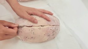 A person's hands score a light pink and purple sourdough loaf with a lame. The unbaked dough, dusted with flour and black sesame seeds, is prepared for the oven on a marble countertop - Powered by Shutterstock - Get 15% off with code: PIKWIZARD15
