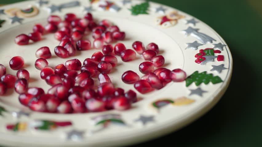 A childs small hand eagerly reaches for bright red pomegranate seeds on a decorative plate, capturing the joy of festive treats enjoyed during family gatherings and celebrations