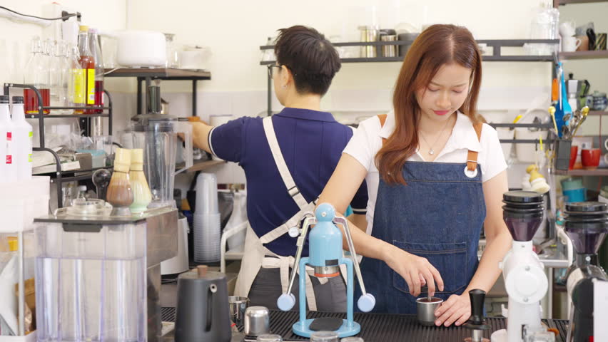 Small business entrepreneur coffee shop cafe. Asian woman barista using manual espresso maker making brewed coffee on bar counter. Waitress working part time job serving beverage drink to customer.