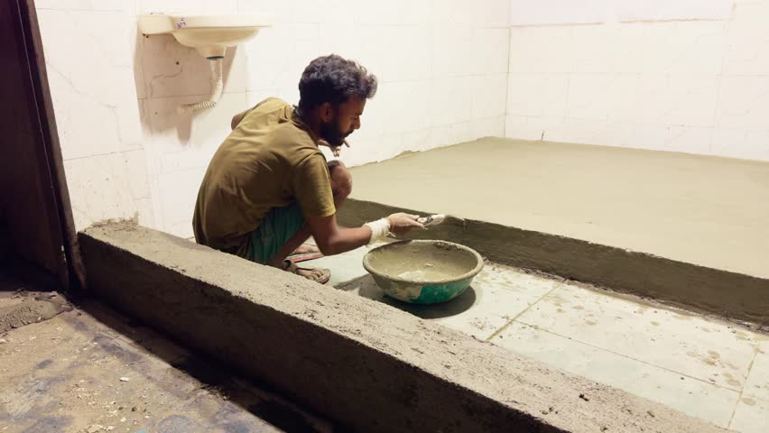 Laborer brushing fresh mix onto floor surface, Mason spreads wet cement on elevated platform in shop, Manual Worker Coats Raised Ground indoor, Expert Applies Bond Layer Inside Commercial Unit, Store