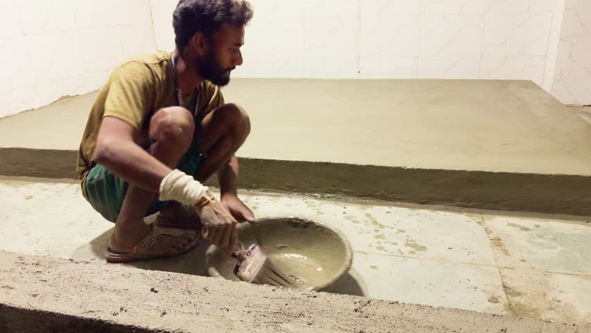 Mason spreads wet cement on elevated platform in shop, Laborer brushing fresh mix onto floor surface, Manual Worker Coats Raised Ground indoor, Expert Applies Bond Layer Inside Commercial Unit, Store
