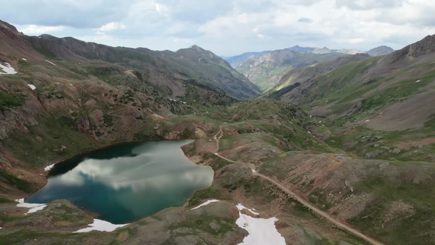 A slow side-moving drone shot of a deep blue glacial alpine lake high in the San Juan Mountains of Colorado in the summertime.