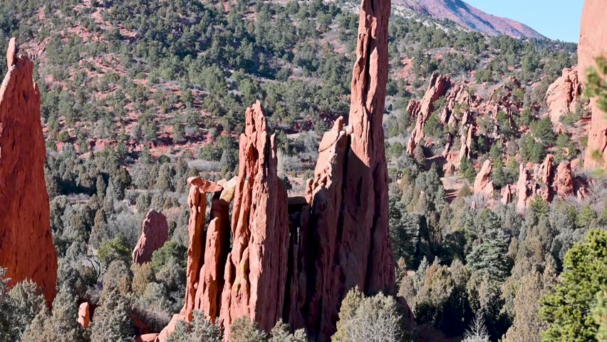 Drone view of tall red sandstone hoodoo rising above forested slopes and distant mountains in Garden of the Gods, Colorado.