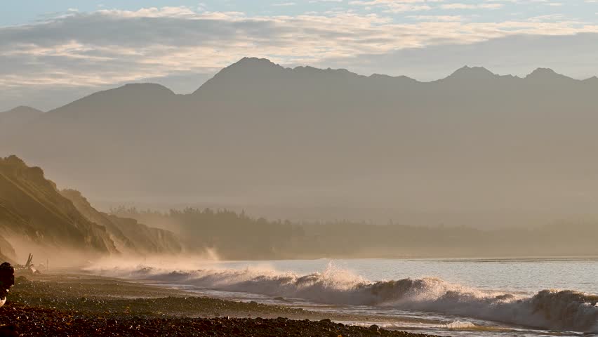 Soft golden mist rolls over a coastal beach backed by dramatic mountain silhouettes in Olympic National Park.
