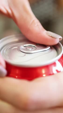A personâs hand opens a red beverage can in a brightly lit indoor setting, captured in a smooth close-up with shallow depth of field