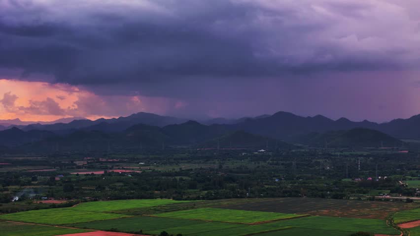 Aerial panoramic view of tropical valley with mountains under glowing purple sky and rain in the distance at sunset