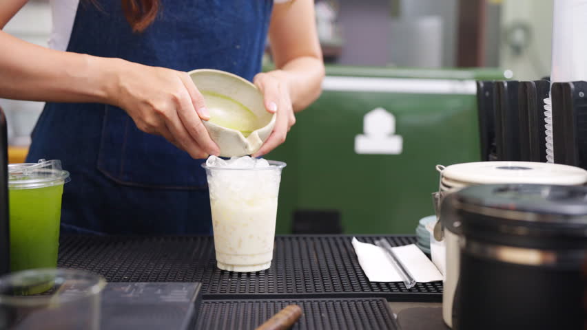 Small business entrepreneur coffee shop cafe and restaurant. Asian woman barista preparing iced matcha green tea latte on bar counter. Waitress working part time job serving beverage drink to customer