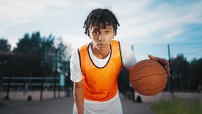 Sportive teen boy playing with ball on streetball court in summer, do sport. Hobby and healthy lifestyle, sport activities for young people, african american teenager looking at camera, champion - Powered by Shutterstock - Get 15% off with code: PIKWIZARD15