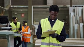 Young african supervisor writing notes on clipboard smiling at camera in carpentry warehouse - Powered by Shutterstock - Get 15% off with code: PIKWIZARD15