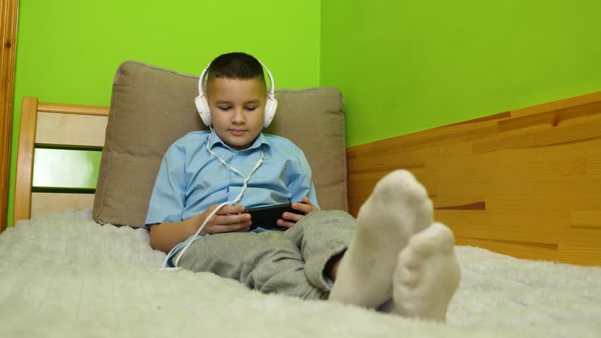 A boy enjoys listening to music from a smartphone with headphones.