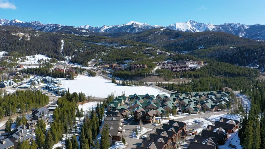 Aerial footage of Big Sky shows condos tucked into a snowy forest landscape, with white roofs, wooded lots, and scenic mountain backdrops filling the quiet Montana winter atmosphere.