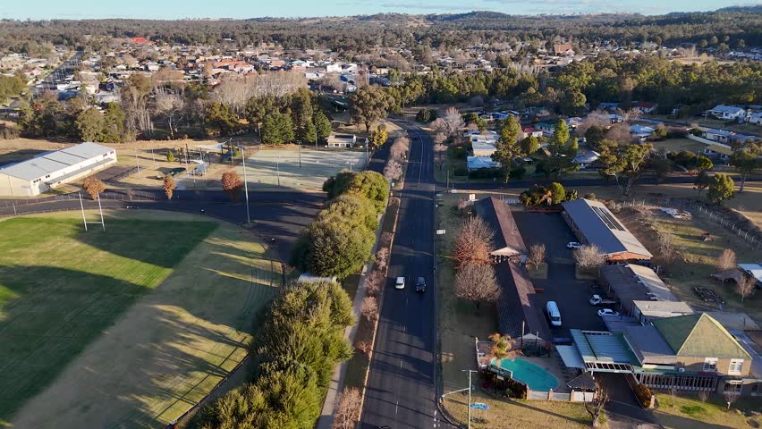 Drone footage follows a car driving along a quiet residential street in a small Australian town, with late afternoon sunlight and clear urban details
