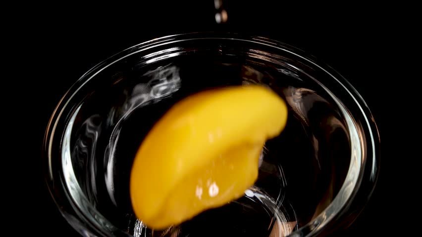 A sliced peach falls into a clear glass bowl with syrup, captured in slow motion against a dark background with dramatic, high-contrast lighting