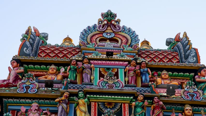 Camera slowly pans down the vibrant, intricately detailed facade of a Hindu temple in Singapore, highlighting ornate statues and vivid architectural elements in daylight