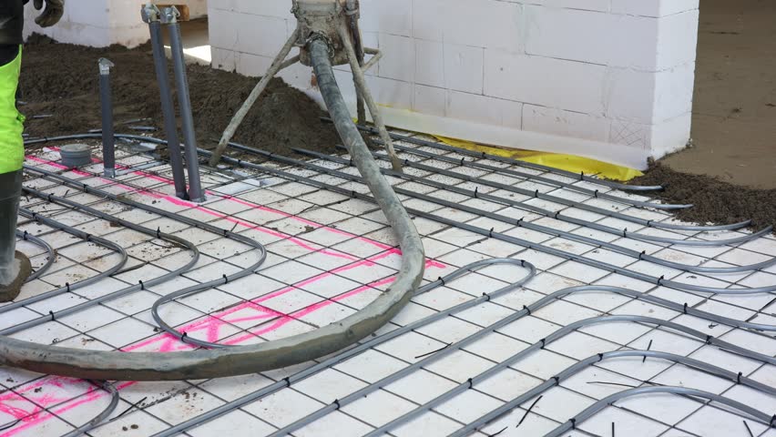 Worker Pouring Concrete Floor in New Building, Construction worker in safety gear pouring concrete over steel reinforcement mesh inside unfinished building, preparing for floor installation.