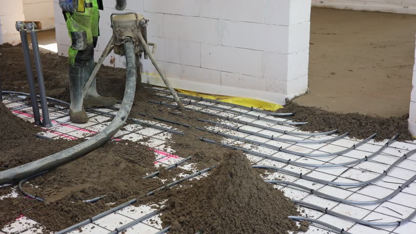 Worker Pouring Concrete Floor in New Building, Construction worker in safety gear pouring concrete over steel reinforcement mesh inside unfinished building, preparing for floor installation.