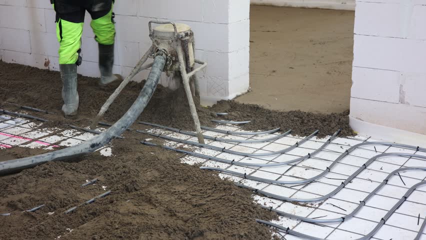 Worker Pouring Concrete Floor in New Building, Construction worker in safety gear pouring concrete over steel reinforcement mesh inside unfinished building, preparing for floor installation.