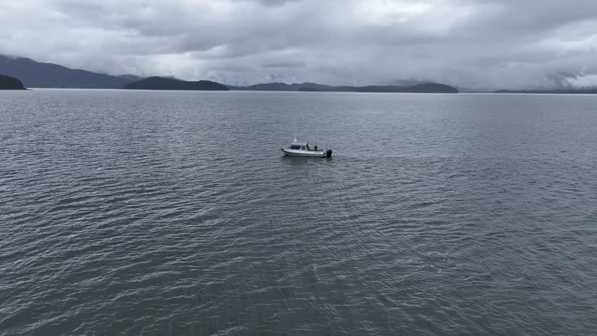 Aerial view of a small white boat on the water, mountains in the background under a cloudy sky, Juneau, Alaska, United States.