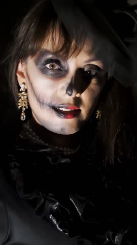 Halloween party, night, frightening portrait of a woman in the twilight, in the rays of light. woman with a terrible make-up in a black witch costume
