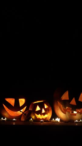 Spooky glowing Jack o lanterns with candle light on rustic table in dark autumn night. Happy Halloween! Scary atmospheric halloween carved pumpkins. Boo! Halloween footage. Trick or treat
