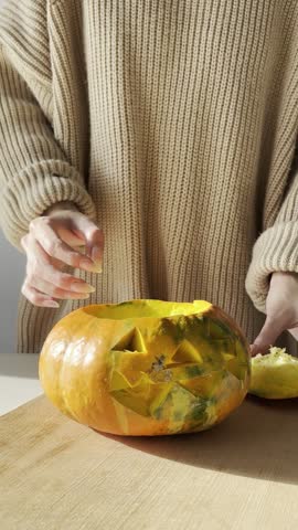 Woman shows finished Halloween pumpkin lantern after carving in bright kitchen. Autumn harvest, festive mood, preparation for the celebration, seasonal home decor