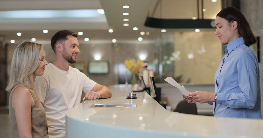 Man and woman walks up to desk and signs papers, takes keys and talks to female. Man signs papers, takes keys and talks to female manager.