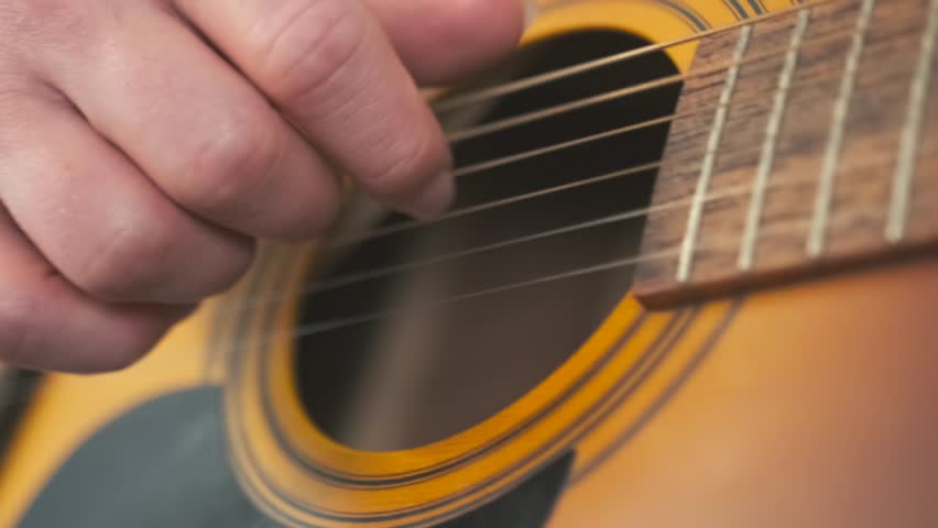 Close-up of a songwriter hand gently plucking the strings of an acoustic guitar in a calm, home environment. Creative moment of composing music.