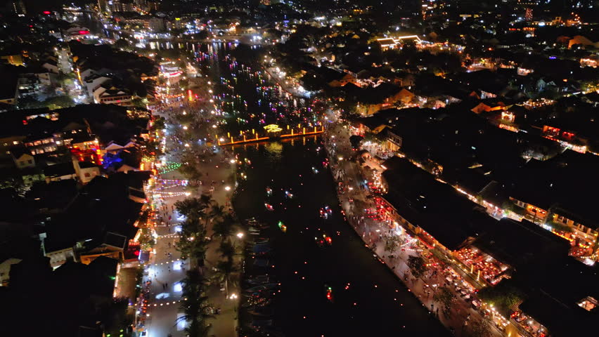 4K aerial view of Hoi An at night with illuminated streets, glowing boats and colorful lanterns along the river.