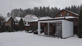 A wooden gazebo with a table, benches and swings stands next to a grassy lawn. Behind it are a fence, trees, buildings and forest. It is snowing heavily in the end of winter. Overcast weather - Powered by Shutterstock - Get 15% off with code: PIKWIZARD15