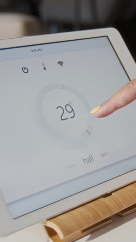 Vertical close up shot of female hand changing temperature using thermostat via smart home tablet control