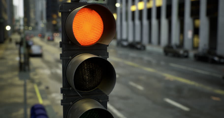 A red traffic signal indicates vehicles must stop at a busy intersection in an urban area during late afternoon. Buildings line the street while cars wait for the light to change.