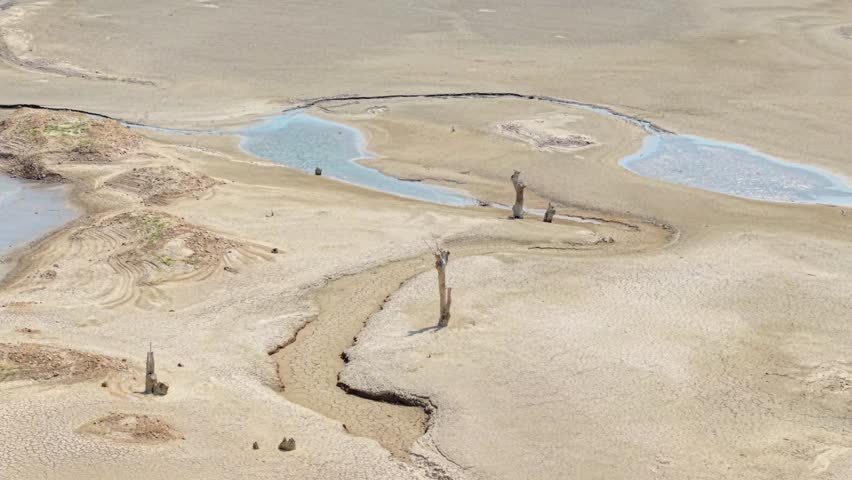 Aerial of curved dry terrain next to low reservoir shoreline in rural Greece area