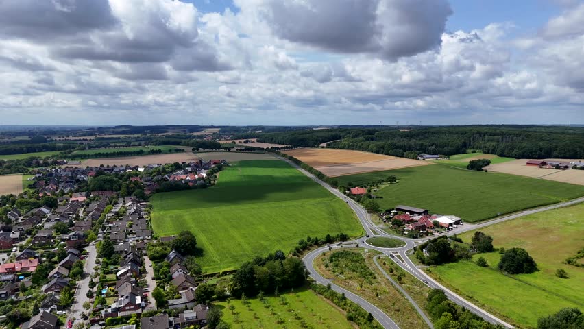 Puffy clouds at blue sky over agricultural farm fields, roundabout and neighborhood. Aerial wide shot. Calm and peaceful landscape of USA. Summer day in August. Farmstead with storage.