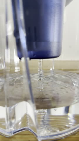 Vertical video - Closeup of clean water dripping through a filter cartridge in a plastic jug, to purify the tap water before drinking it.
