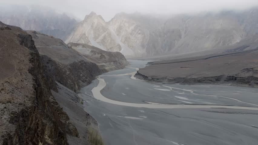 Aerial View of a Serene River Valley in Pakistan, Surrounded by Majestic Mountains and Clouds