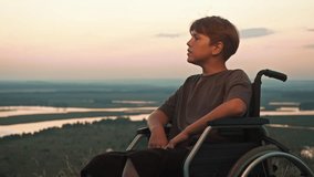 Teenage boy in wheelchair enjoys beautiful view of sunset, watching it from hill that overlooks natural fields and horizon of river. - Powered by Shutterstock - Get 15% off with code: PIKWIZARD15