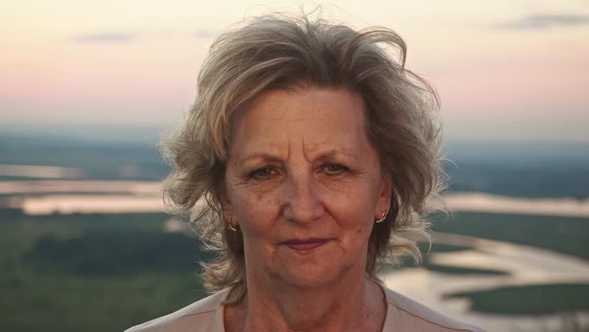 Portrait of active young woman, or grandmother or pensioner, with light makeup, against backdrop of a summer sunset.