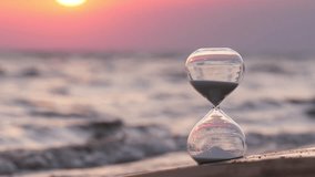 White sand hourglass resting on sandy beach, measuring passing time with sea waves and vibrant sunset glowing on background. Selective focus on sand glass on foreground, background in bokeh blur - Powered by Shutterstock - Get 15% off with code: PIKWIZARD15