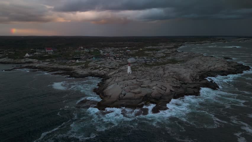 Cinematic Drone Shot on Peggys Cove Lighthouse Nova Scotia. The Rugged Beauty Of Nova Scotia Coast Seen From The Sky As Waves Dance Around Historic Lighthouse During Sunset Hour.