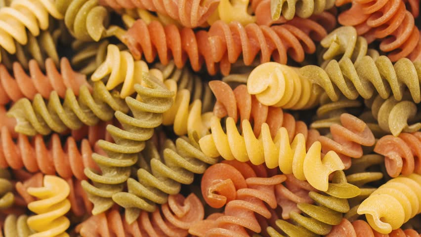 Vibrant dry spiral pasta pieces in green, yellow, and orange colors are closely arranged together creating a delicious food background texture.