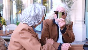 Senior couple sits at an outdoor cafe table under a sunny arcade, one hand holding a red credit card against a wireless card reader as they laugh together,sunglasses today on terrace  - Powered by Shutterstock - Get 15% off with code: PIKWIZARD15