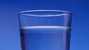 Slow motion slo mo in studio lightings as multiple ice-cubes and ice fall and drop into glass cup full of water liquid and spills, splash, bubble, and drip from top of refreshment container with blue - Powered by Shutterstock - Get 15% off with code: PIKWIZARD15