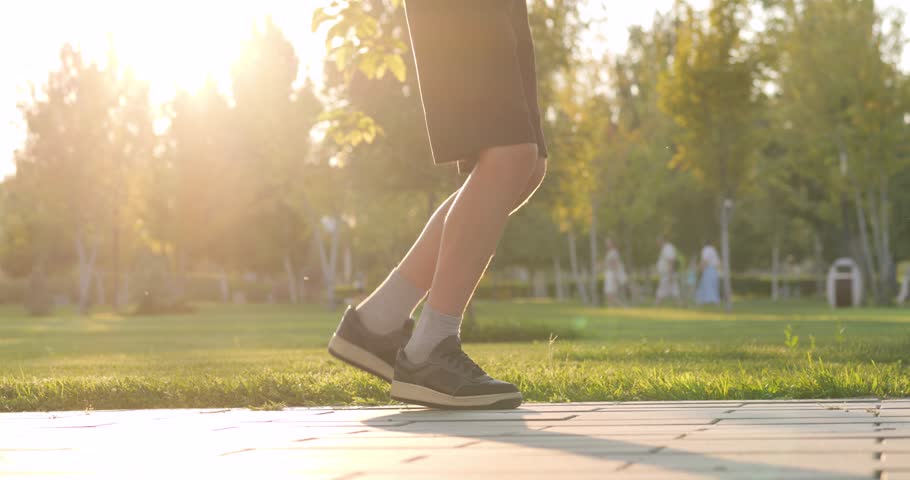 Baby jumps rope outdoors during golden hour. Close-up toddlers legs in shorts sneakers show energy joy. Baby plays happily nature sunset. Jumping toddler loves movement. Child enjoys fitness outdoors