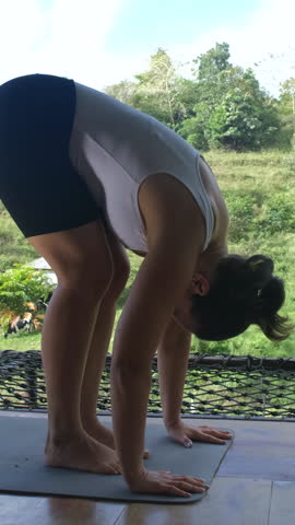 Vertical video. Woman practicing yoga by rice plantations and tropical greenery on a bamboo terrace, slow motion 