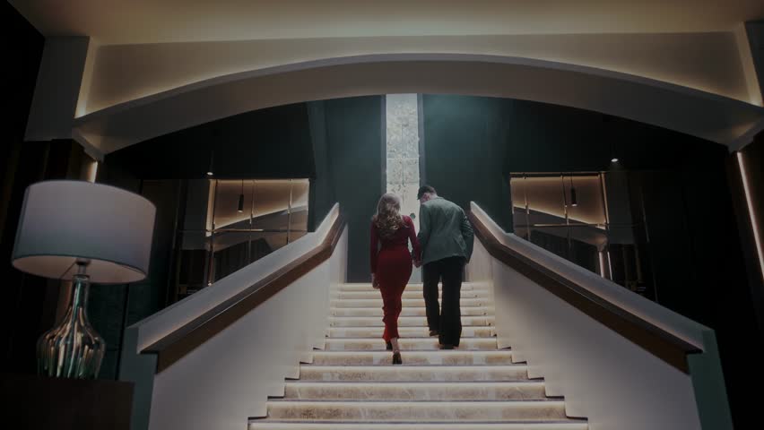 Smartly dressed man and woman walk together up the stairs to the terrace of an upscale restaurant during a romantic date