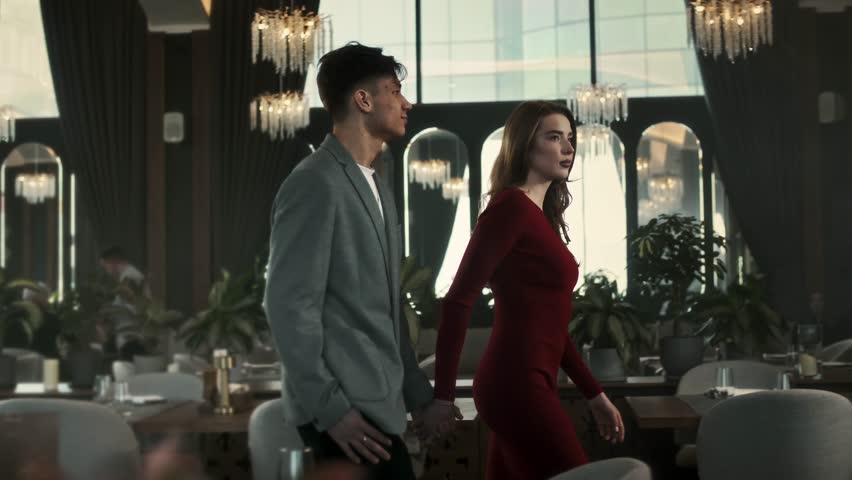 Young lovers walk together through the large hall of a beautiful restaurant among tables and indoor plants